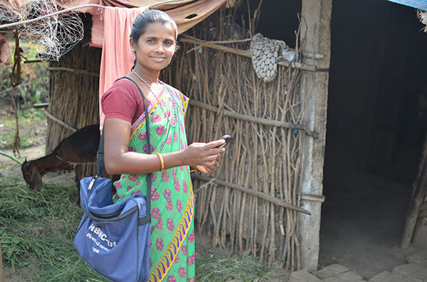 ASHA smiling and holding her smartphone as she enters the home of a patient in rural India.
