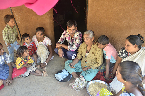 A village family in Gujarat sitting on the floor while an ASHA accesses the ImTeCHO app on a smartphone.
