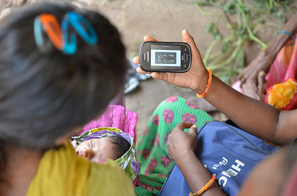 An ASHA shares a view of her smartphone and the ImTeCHO app with a young mother and her baby.
